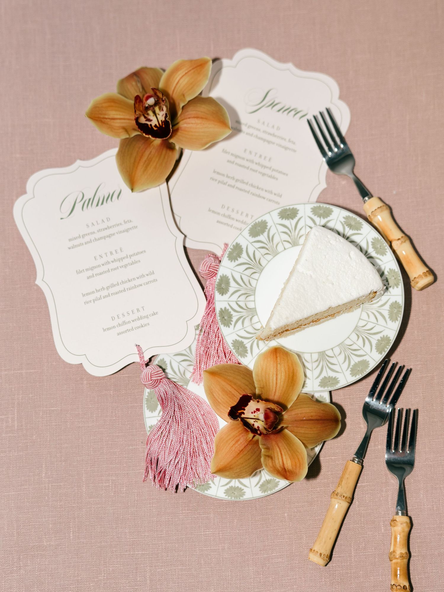 Elegant wedding menu cards with gold orchids and pink tassels arranged on a beige linen tablecloth.