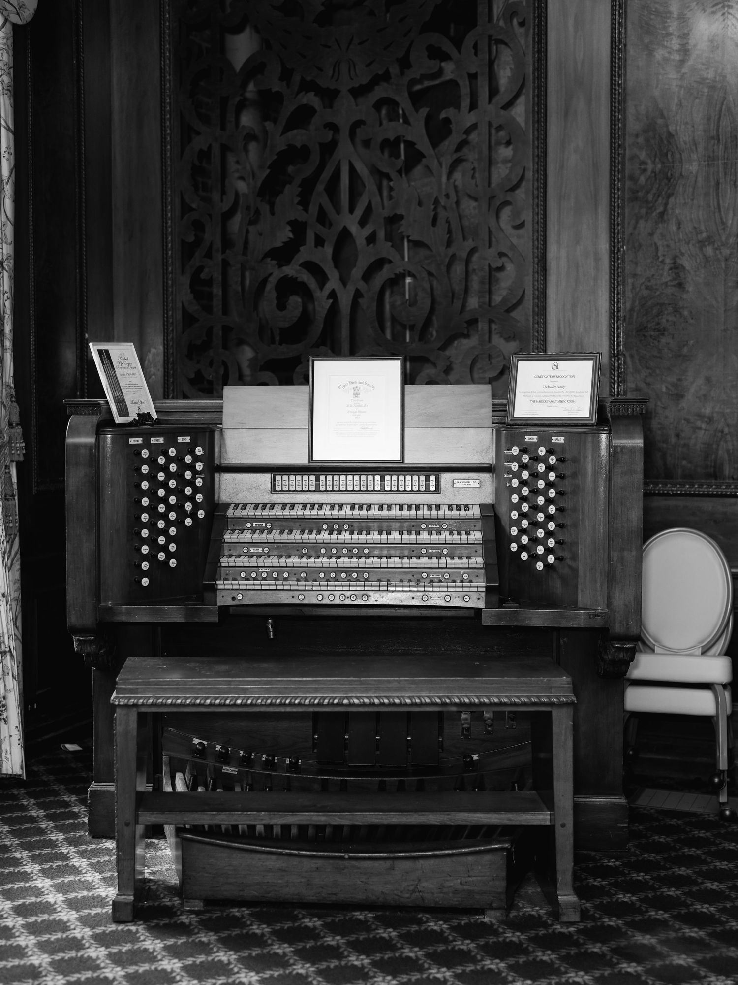 A vintage church organ console with multiple keyboards and stops in black and white, positioned in an ornate interior setting.