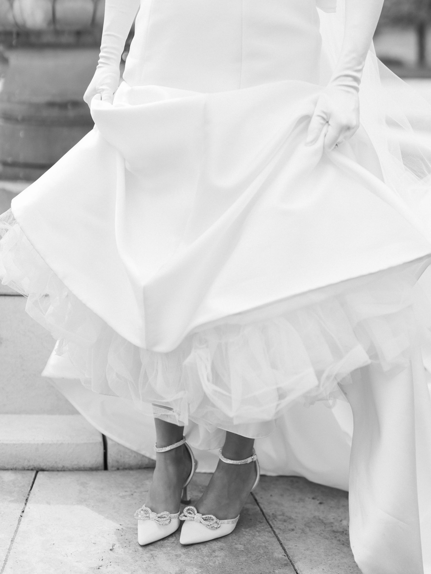 Black and white photo series showing close-up details of a bride's white shoes and dress hem on stone pavement.