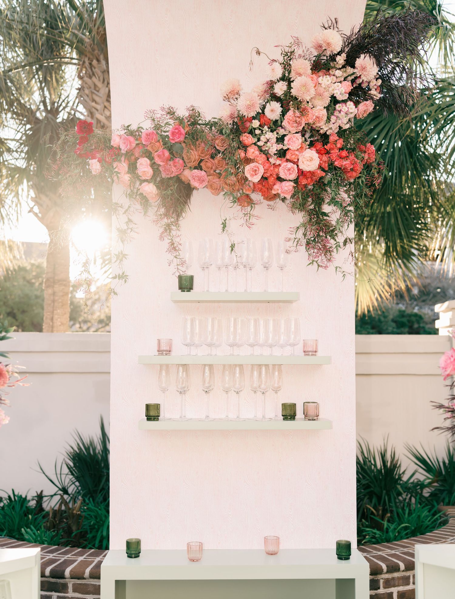 Romantic outdoor wedding venue with white walls, hanging lanterns, and pink floral arrangements at sunset.