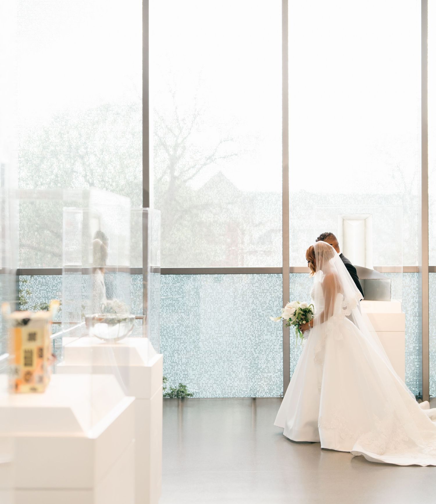 A dreamy bridal photo session with elegant white gowns against large windows in a bright, airy studio space.