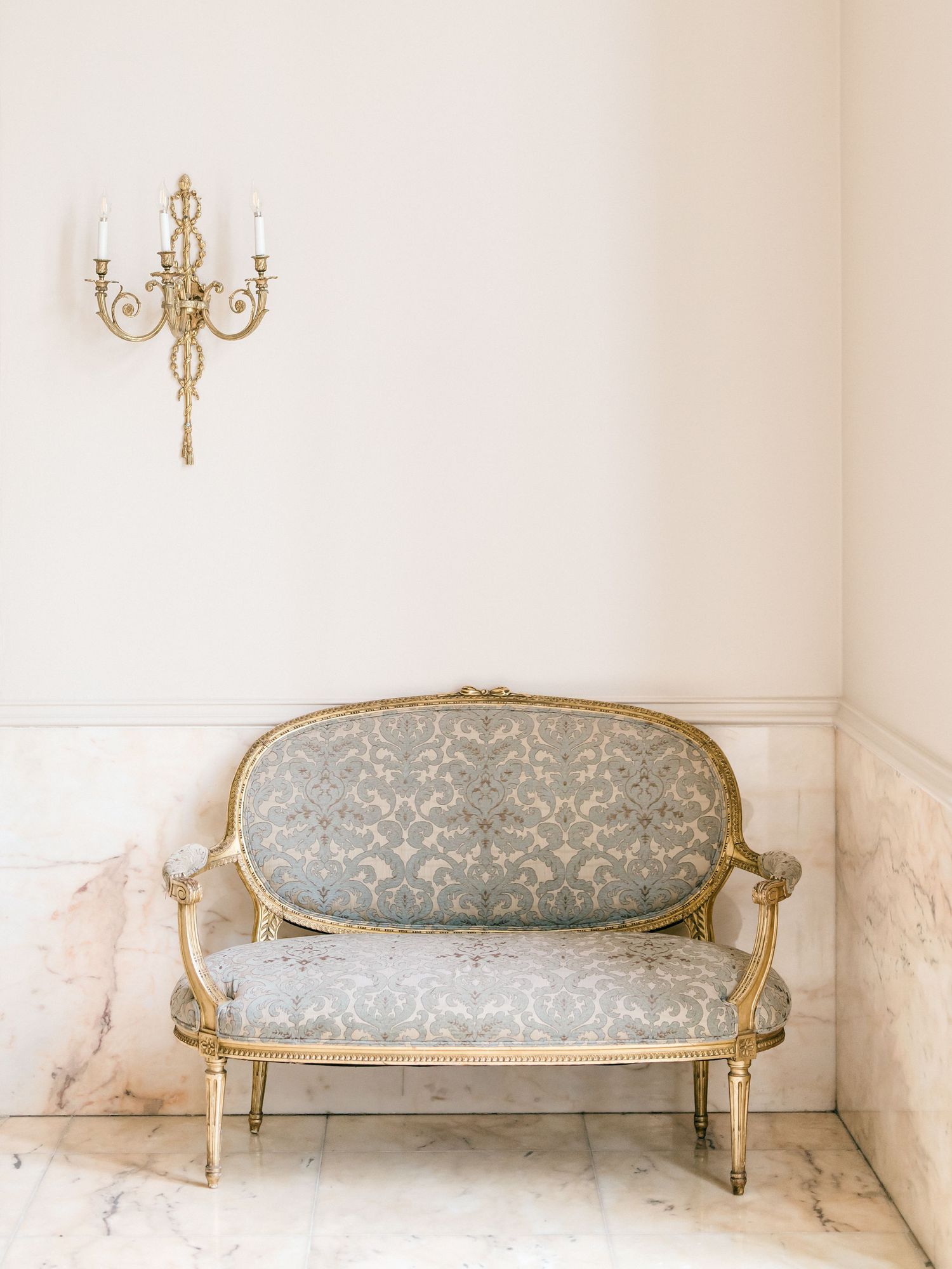 Elegant vintage French style settee with ornate gold frame and light blue damask upholstery displayed in a white room.