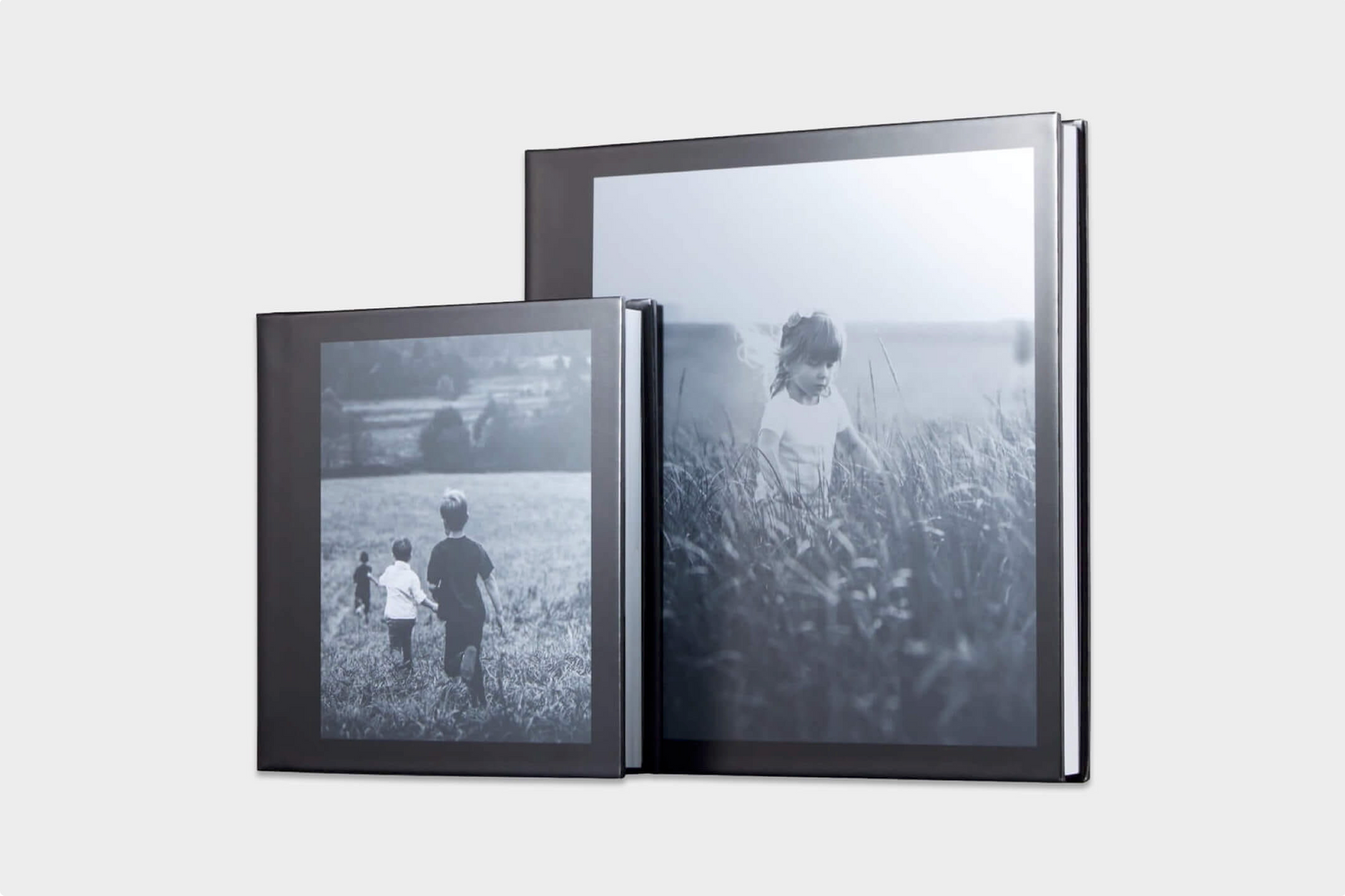 Two black photo albums of different sizes displaying vintage black and white photographs of figures in fields or meadows.