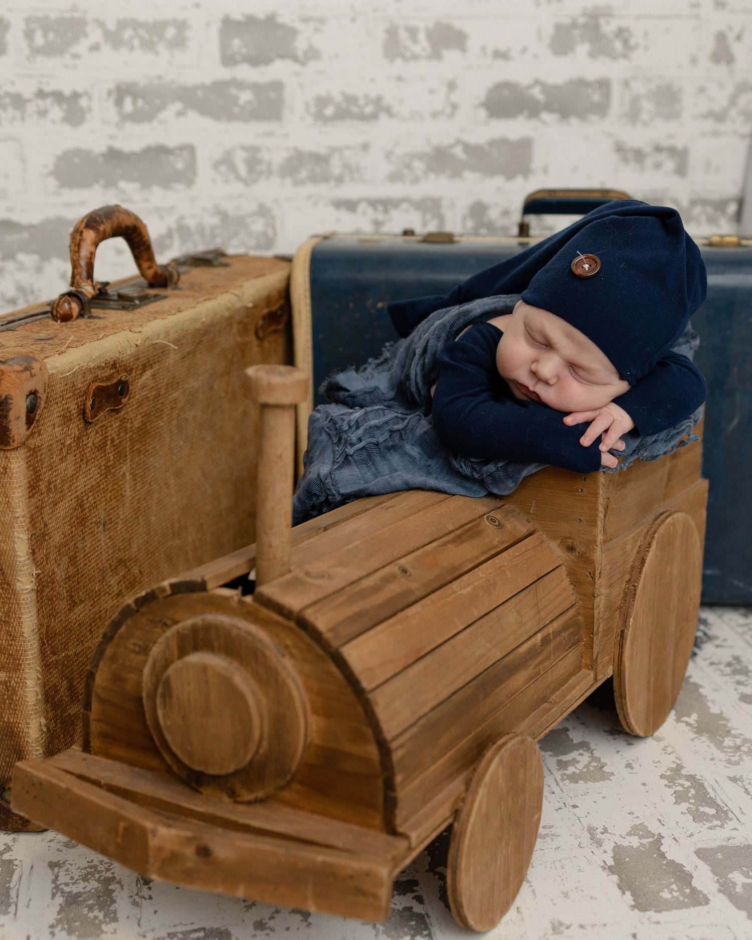 A rustic wooden toy vintage car with a cozy wrap serves as a unique baby photography prop against a white brick wall.
