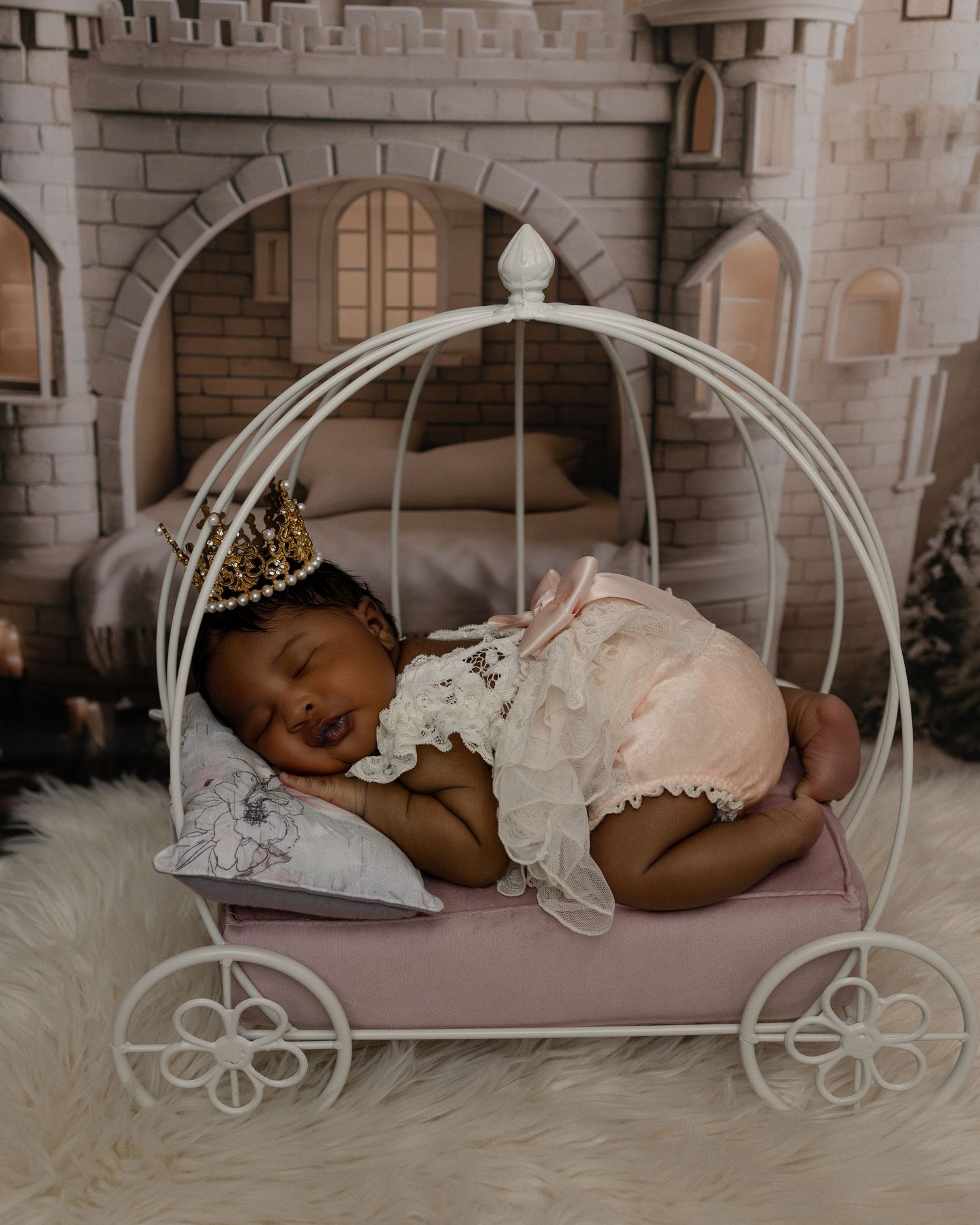 Baby sleeping peacefully in a decorative white carriage prop with castle backdrop and wearing delicate lace dress.