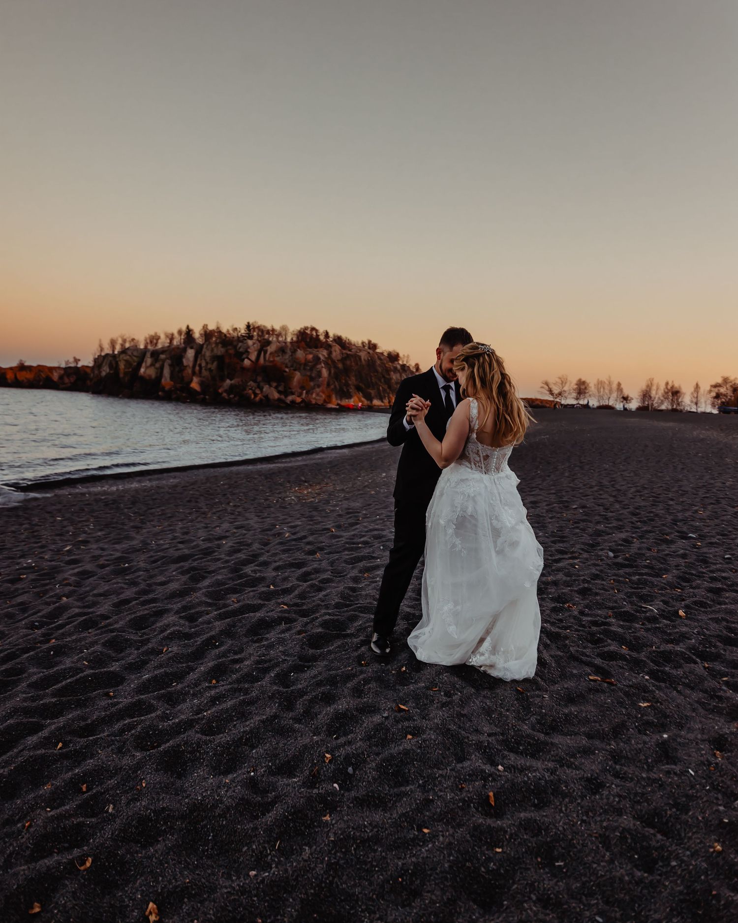 A couple shares a romantic moment on a black sand beach at sunset. during their elopement