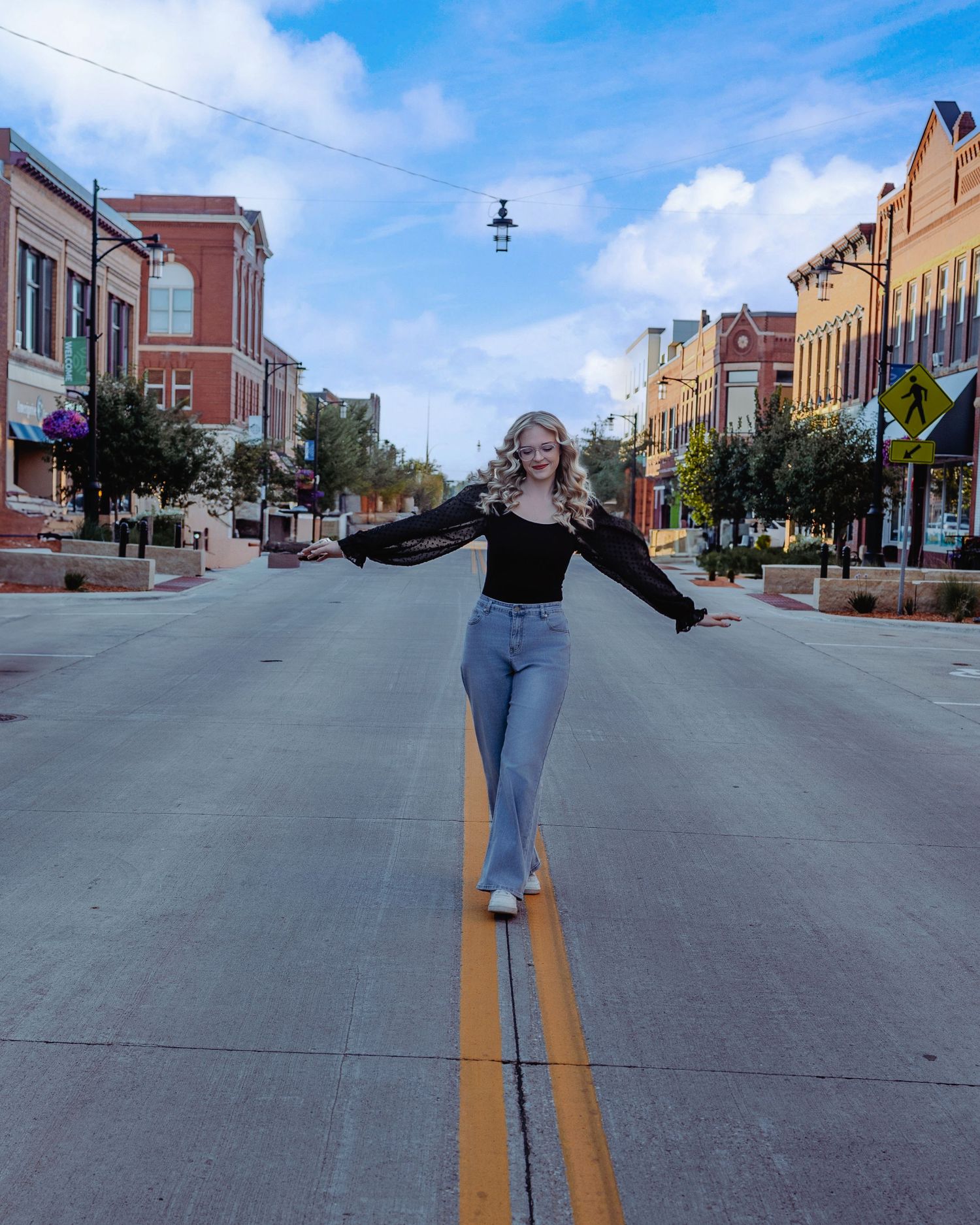 Person balances on double yellow lines in historic downtown district with brick buildings and blue sky overhead.