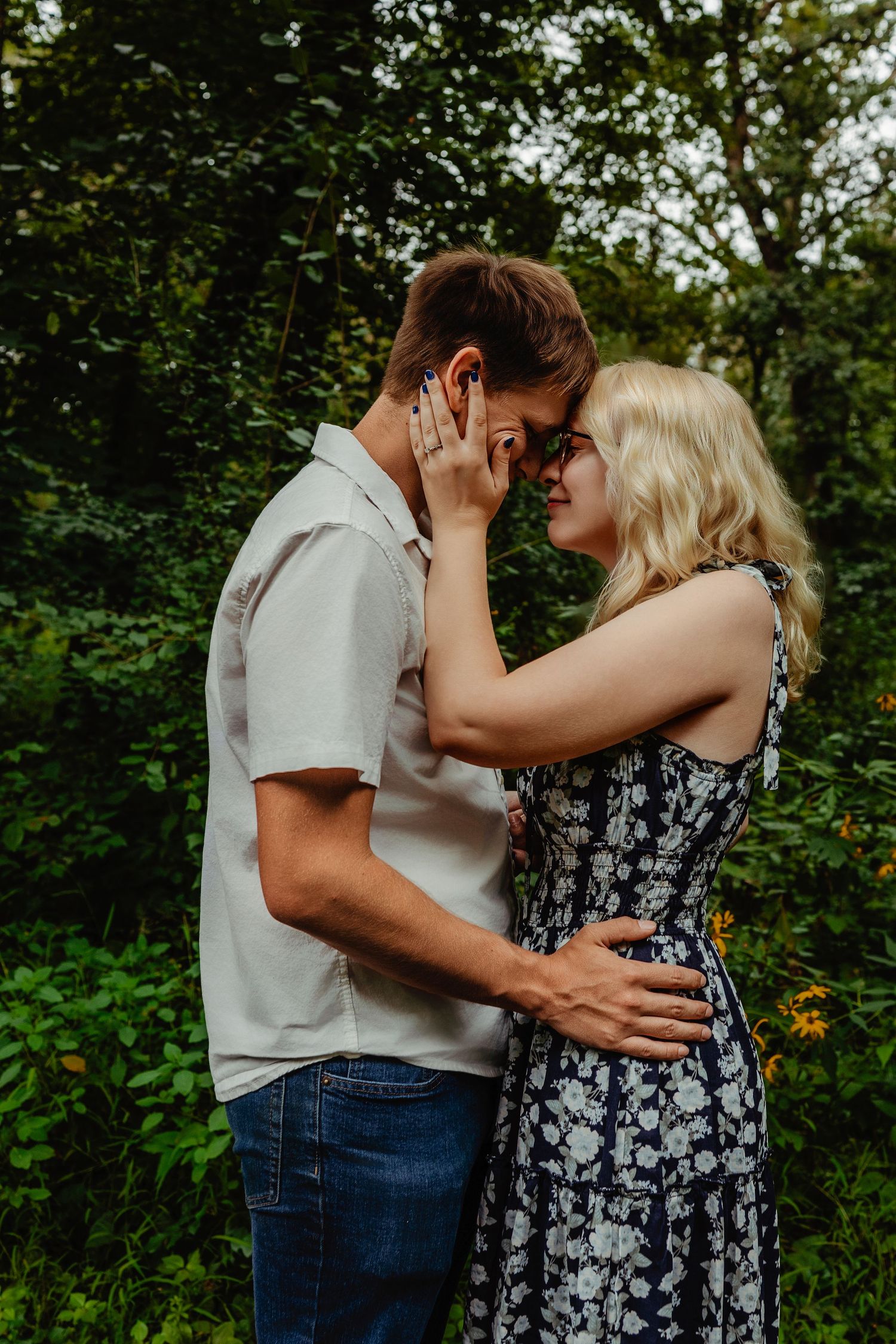 Romantic couple embraces in nature setting with lush green foliage background during intimate outdoor photo session.