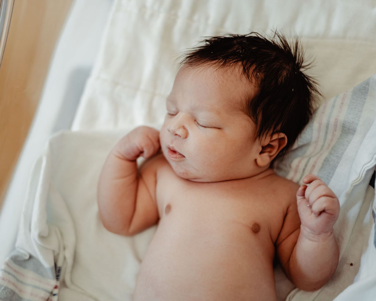 Peaceful sleeping newborn with dark hair lying on white hospital linens.