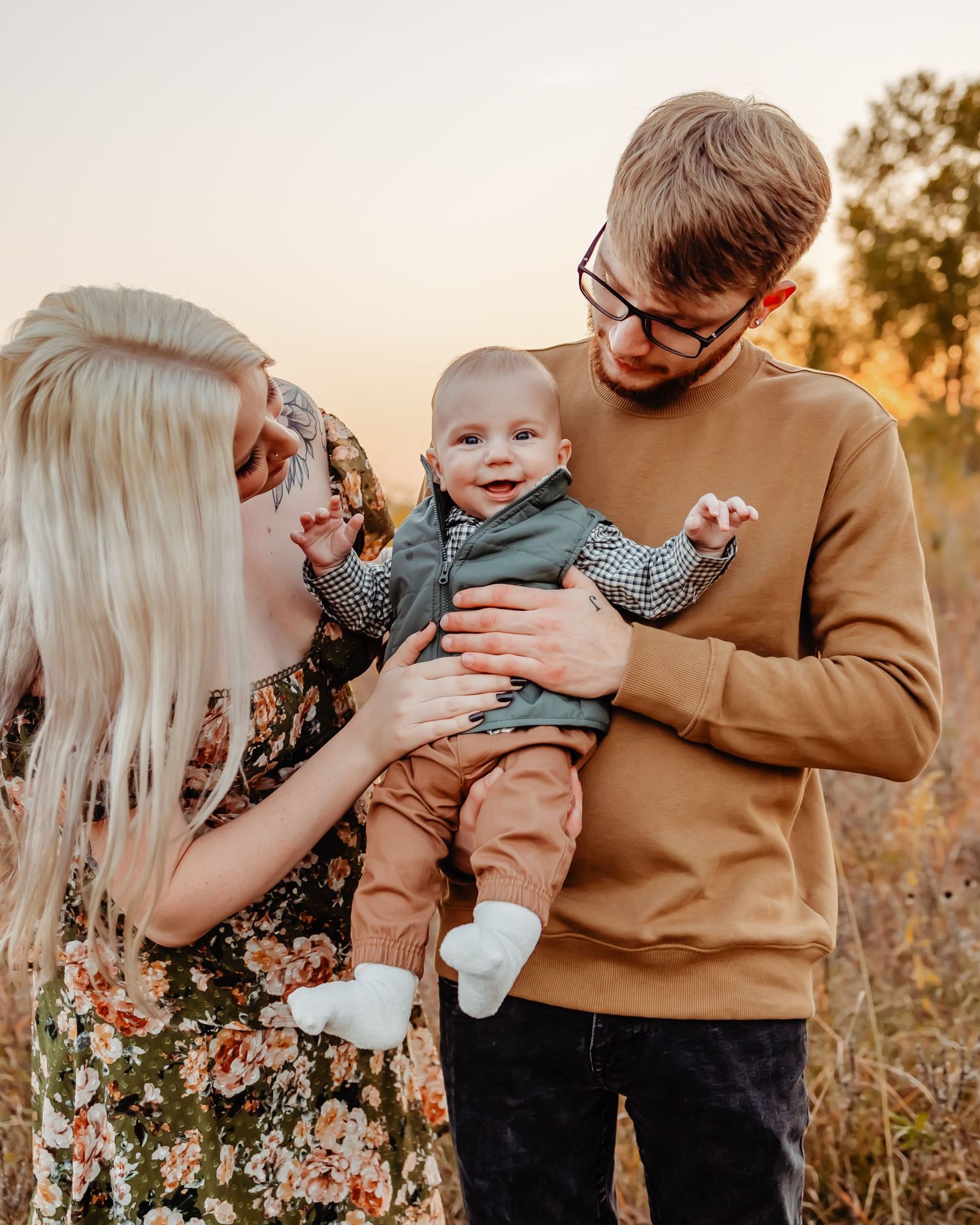 Heartwarming family portrait in golden sunlight with their happy baby dressed in casual autumn attire.