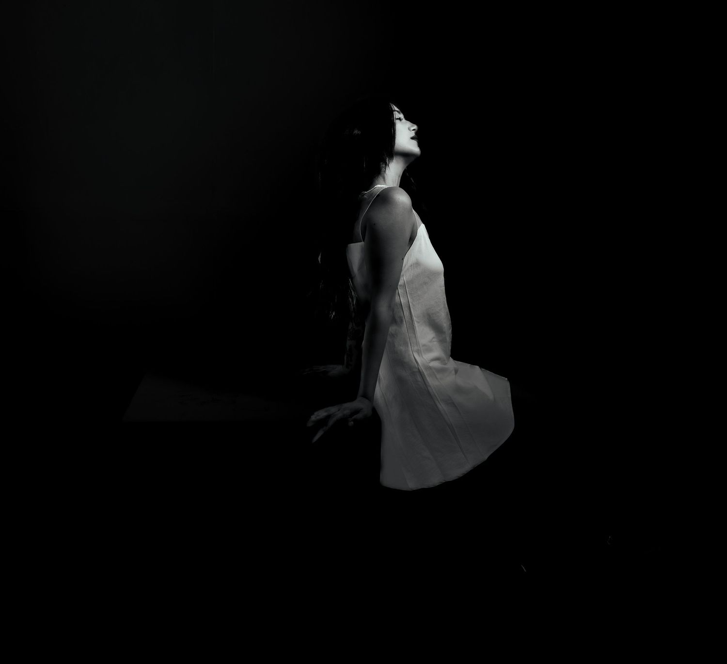 A woman in a white dress poses gracefully against a dark background in a dramatic black and white photo.