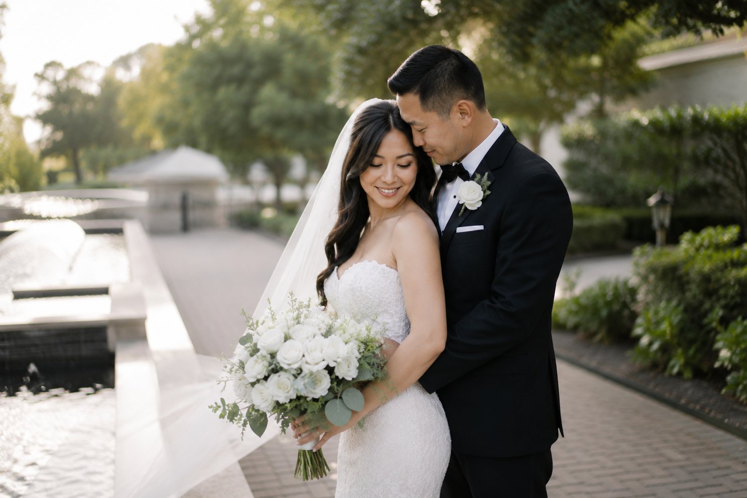 Bride and groom share a romantic moment outdoors, bride holding white floral bouquet in elegant strapless gown.