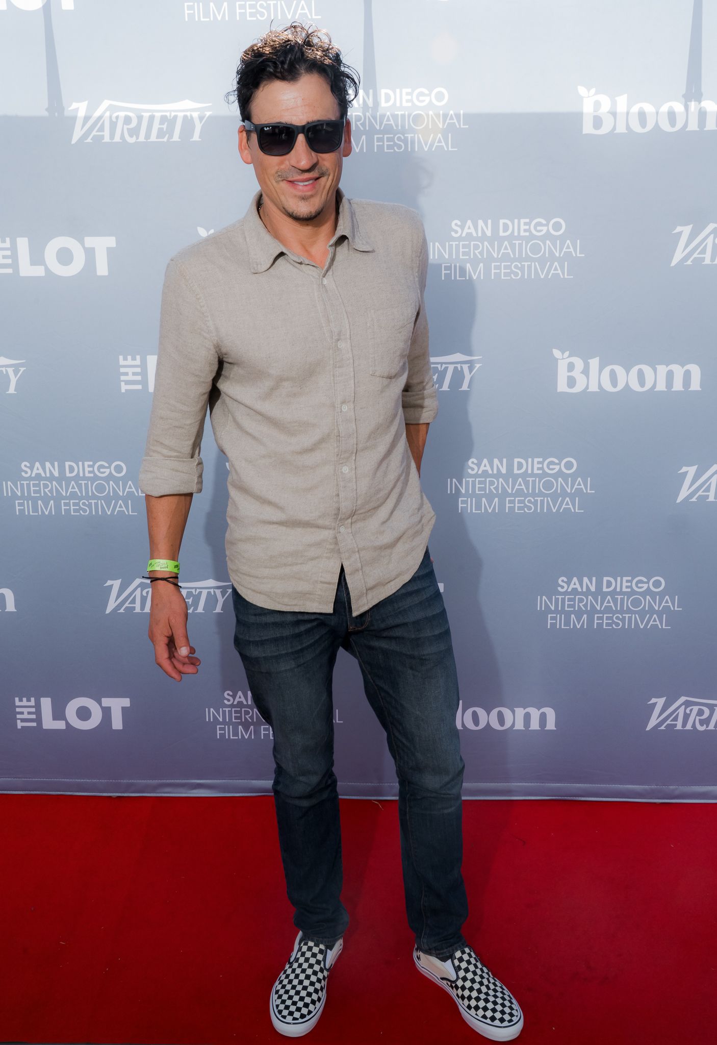 Man in gray shirt, jeans, and checkered Vans poses on red carpet at San Diego International Film Festival.