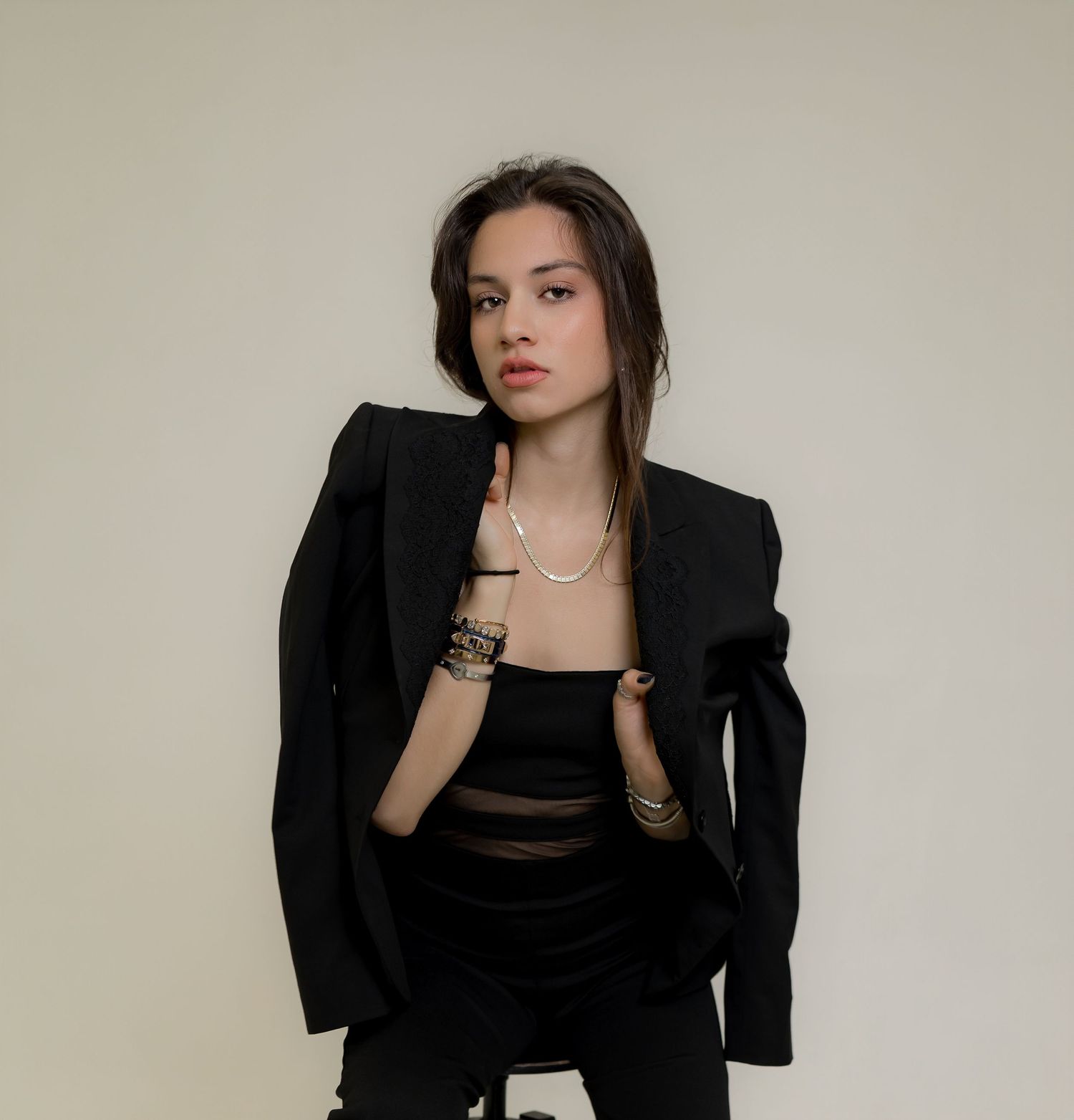 Young woman in black blazer and tube top with pearl necklace and layered bracelets posing confidently.