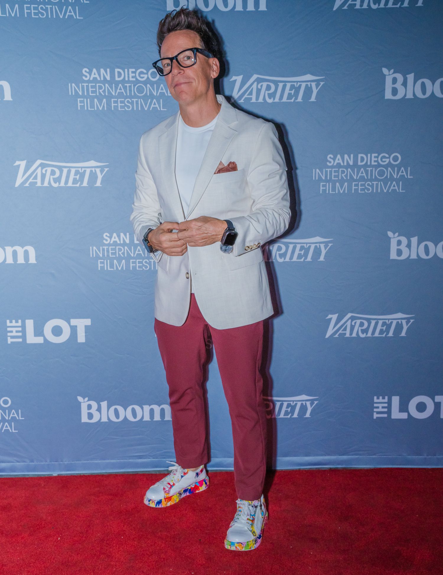Man in white blazer, red pants, and colorful sneakers poses on red carpet at San Diego International Film Festival.