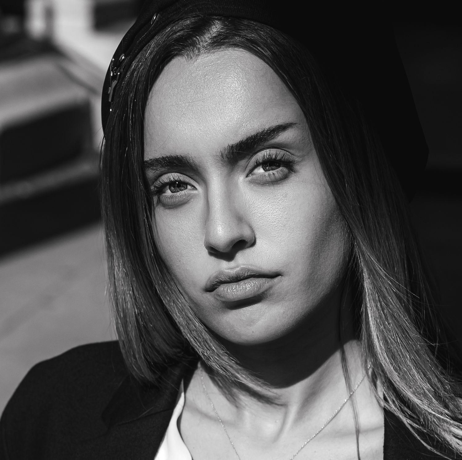 Black and white portrait of a young woman with straight hair, gazing directly at the camera in natural sunlight.