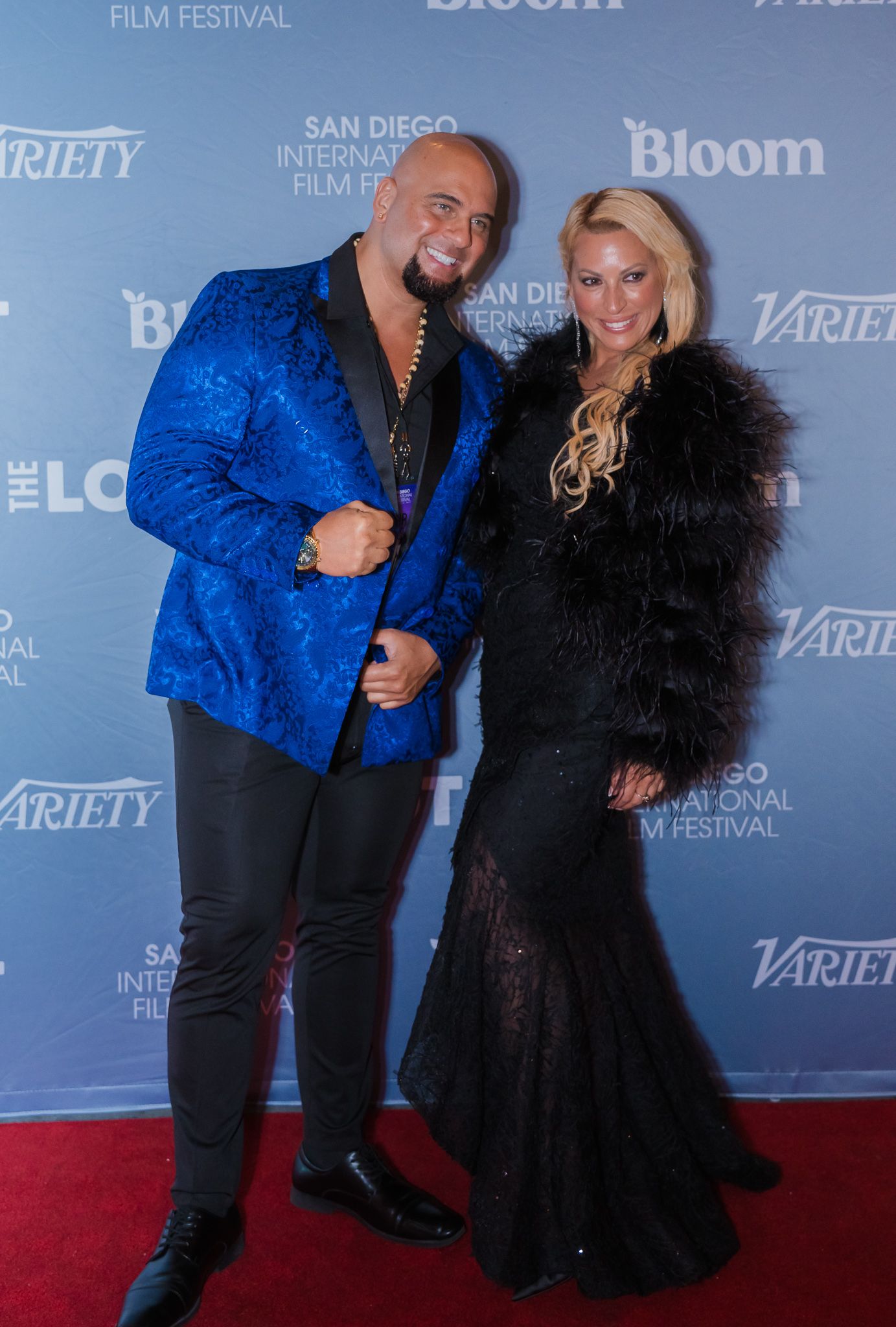 A man in a blue blazer and a woman in a black gown pose on the red carpet at the San Diego International Film Festival.