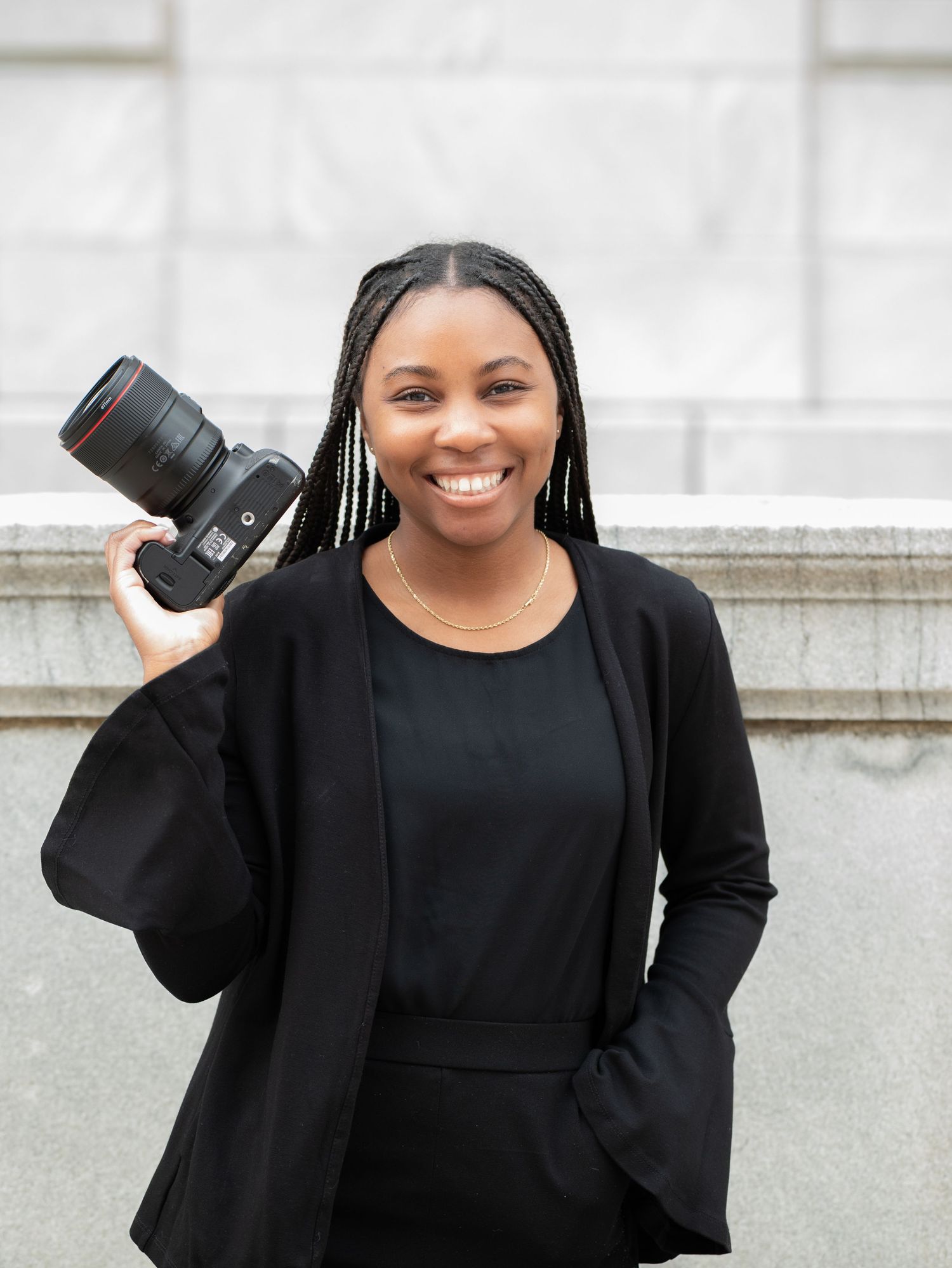 Young woman in black outfit holding professional camera outdoors.