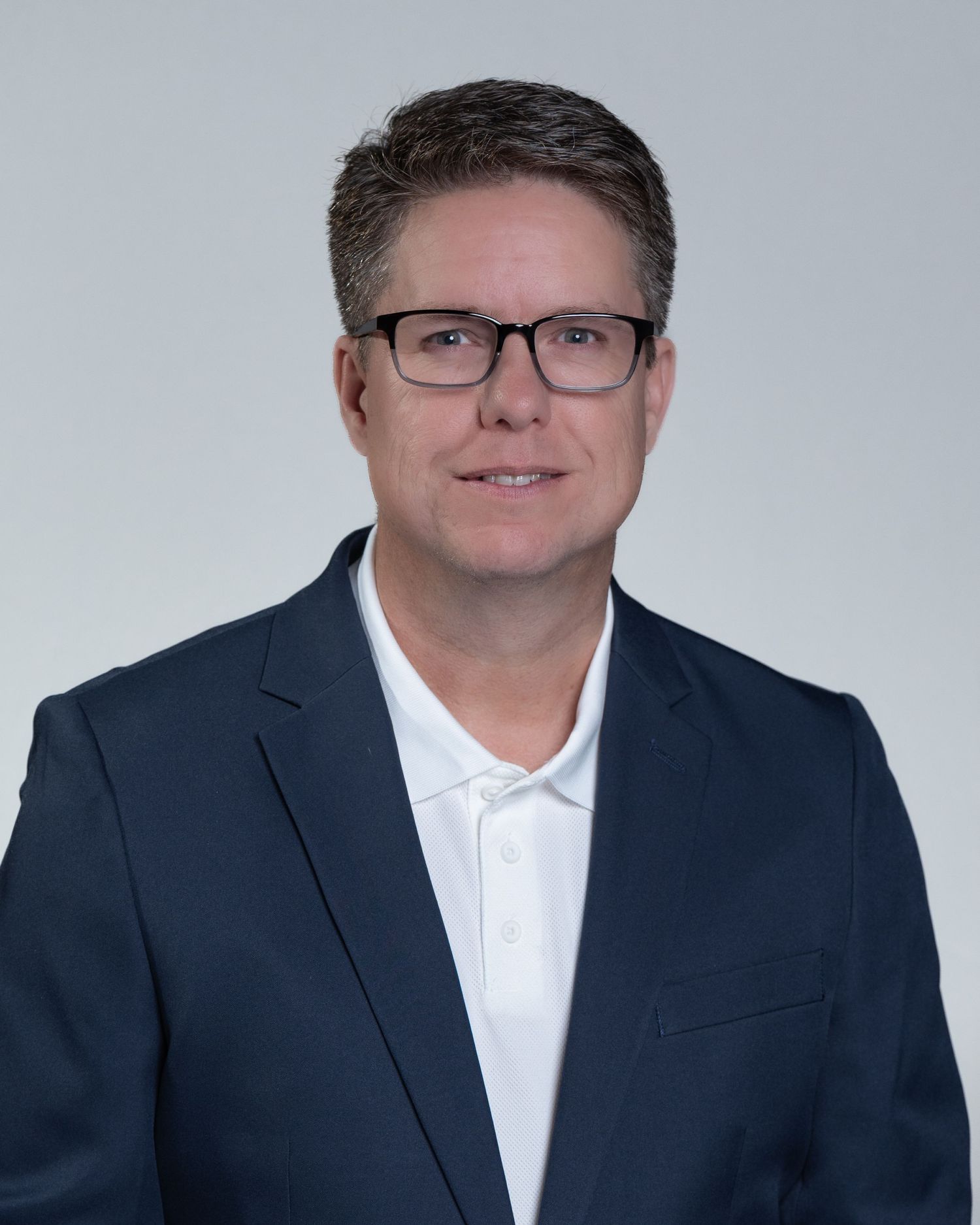 Middle-aged man wearing glasses and navy blazer smiles for professional business headshot photo.