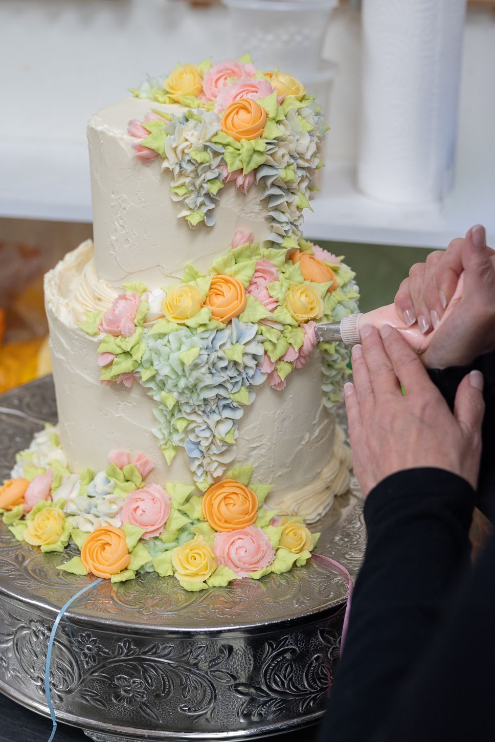 Two-tier white wedding cake decorated with colorful buttercream flowers being cut by couple.