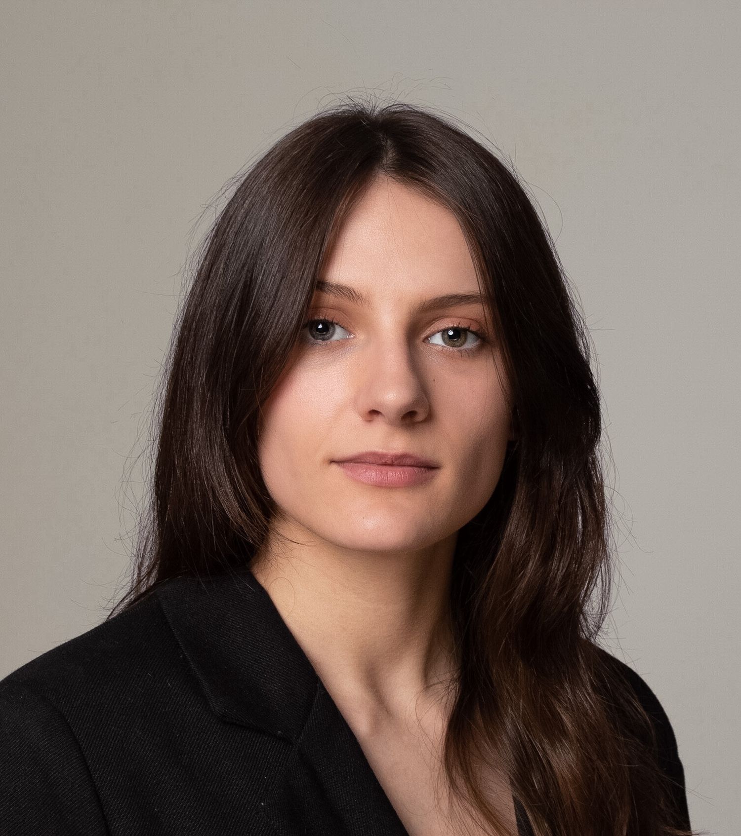 Young woman with long brown hair wearing black blazer poses for professional headshot photo.