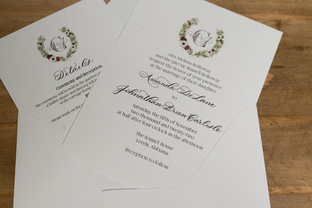 Elegant wedding invitation suite with monogram wreath design displayed on a wooden surface.