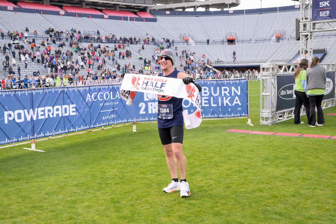 Athlete crosses finish line at a marathon event in a stadium, holding a banner.