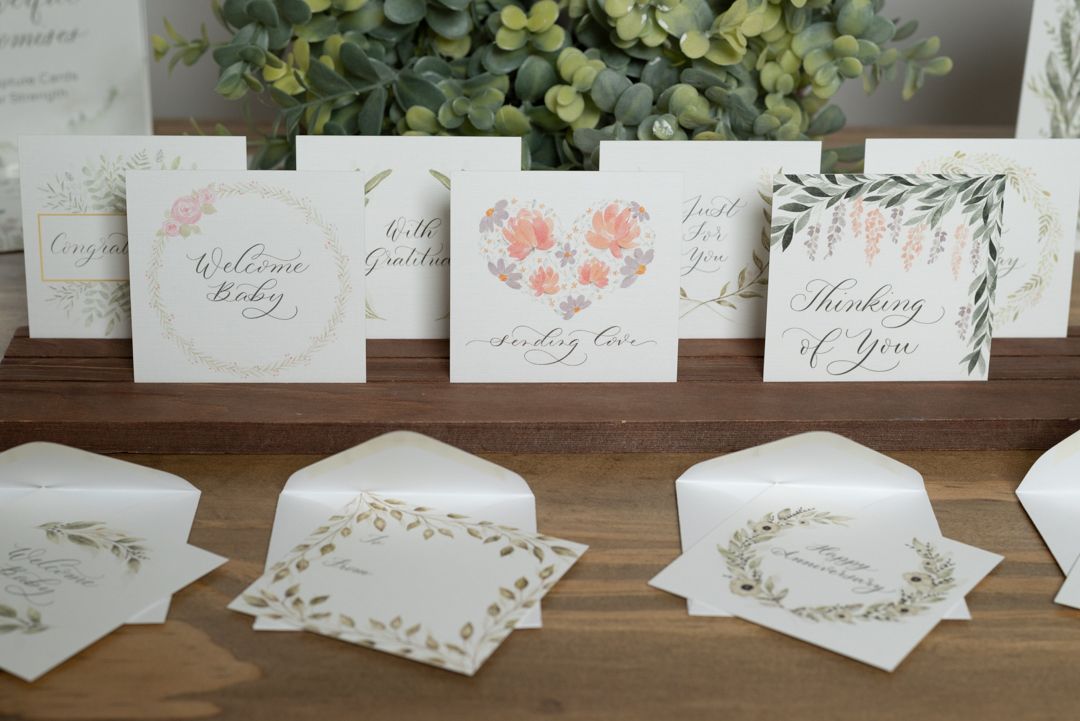 A collection of elegant floral greeting cards with matching envelopes displayed on a wooden surface with greenery.