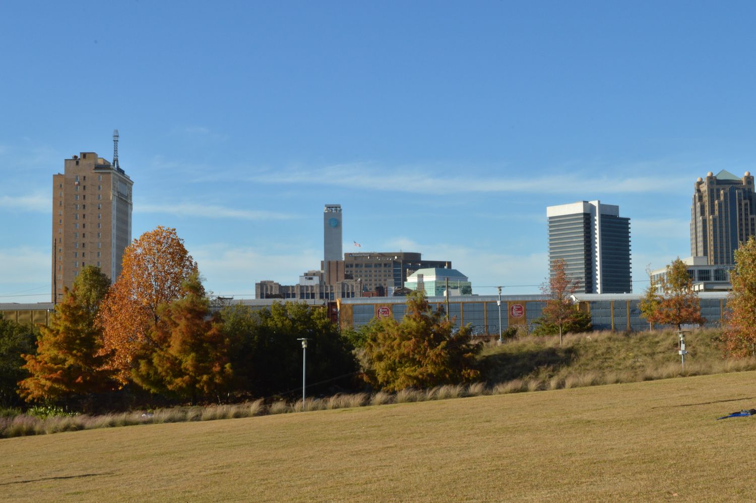 Autumn cityscape with colorful trees and modern skyscrapers under a clear blue sky viewed from a grassy park.