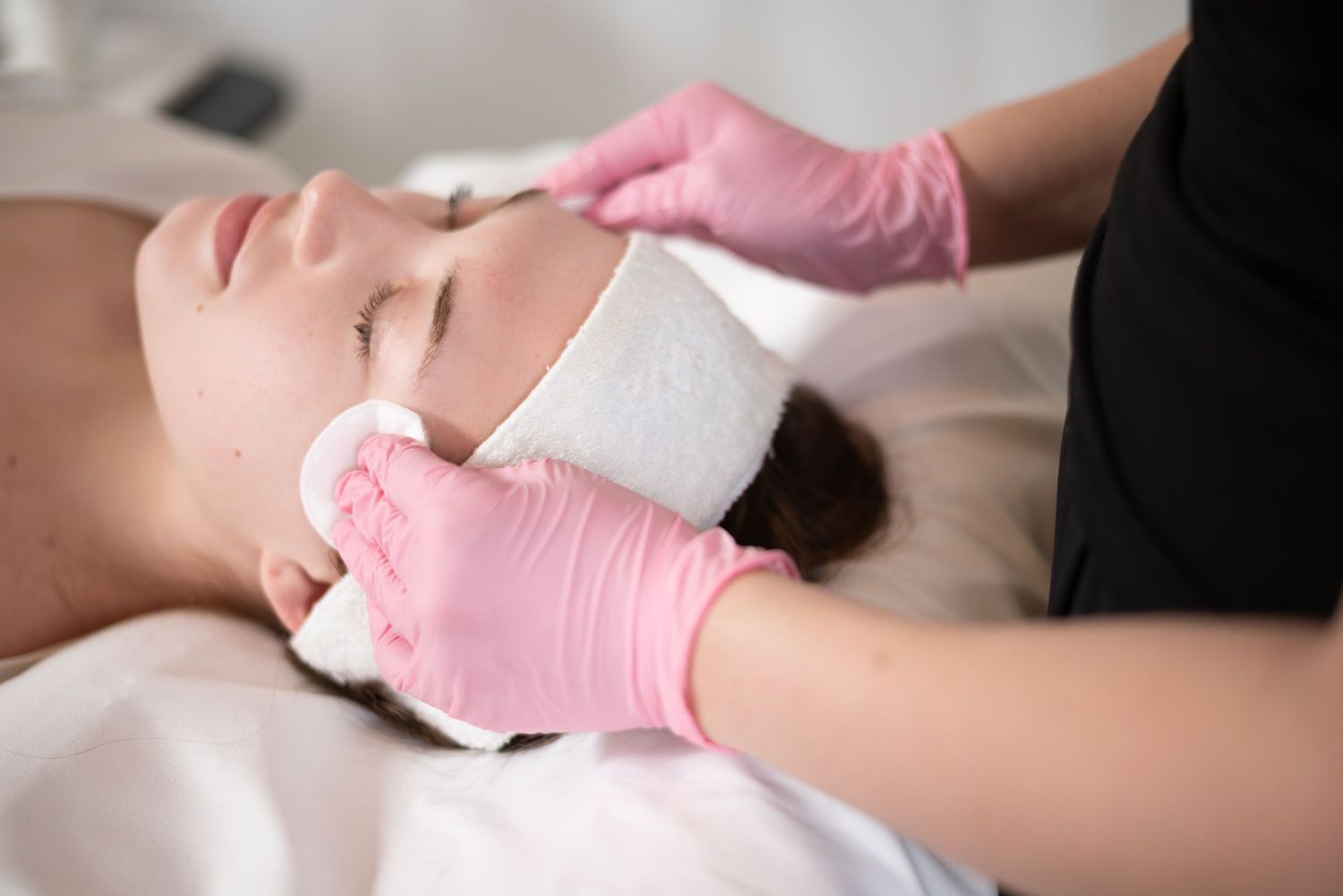 Esthetician in pink gloves performing professional facial treatment on relaxed female client.