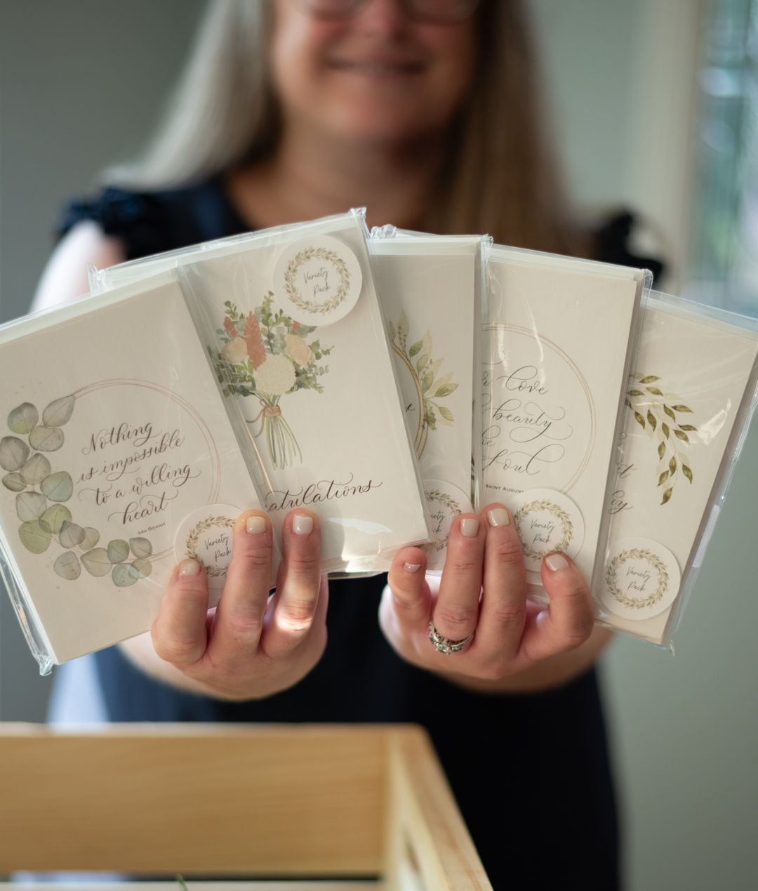 Woman holding four elegant floral greeting cards with congratulations messages, displayed in a wooden box.