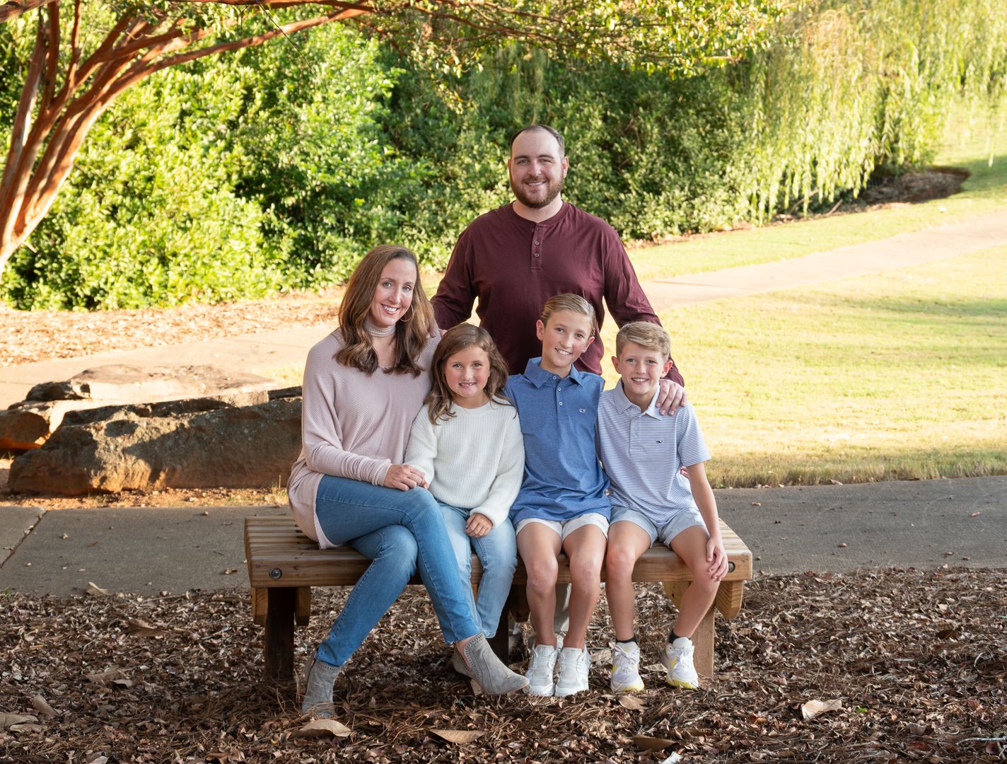 Happy family of five posing on bench under tree in outdoor fall portrait session.