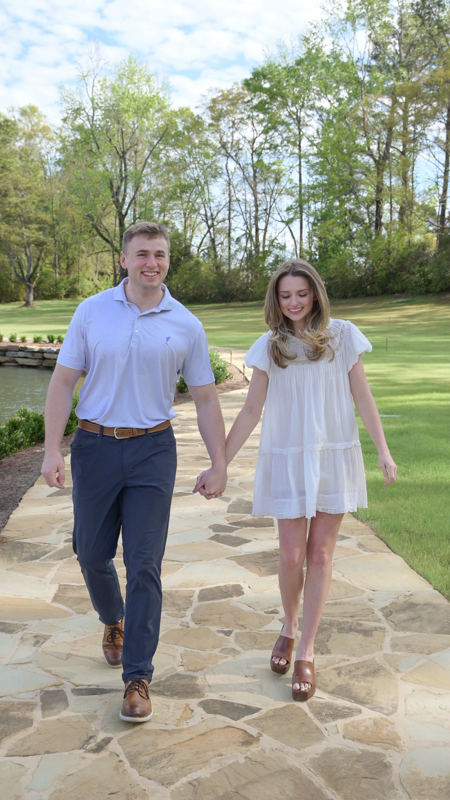Young couple holding hands walking on stone path through lush green park setting outdoors.