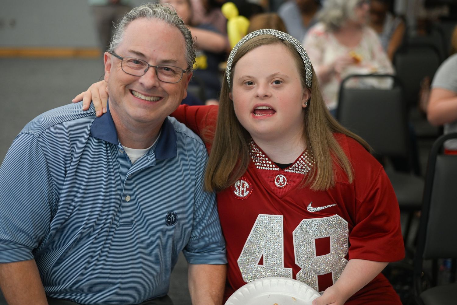 Man and young woman in Alabama jersey #48 smiling together at an indoor event.