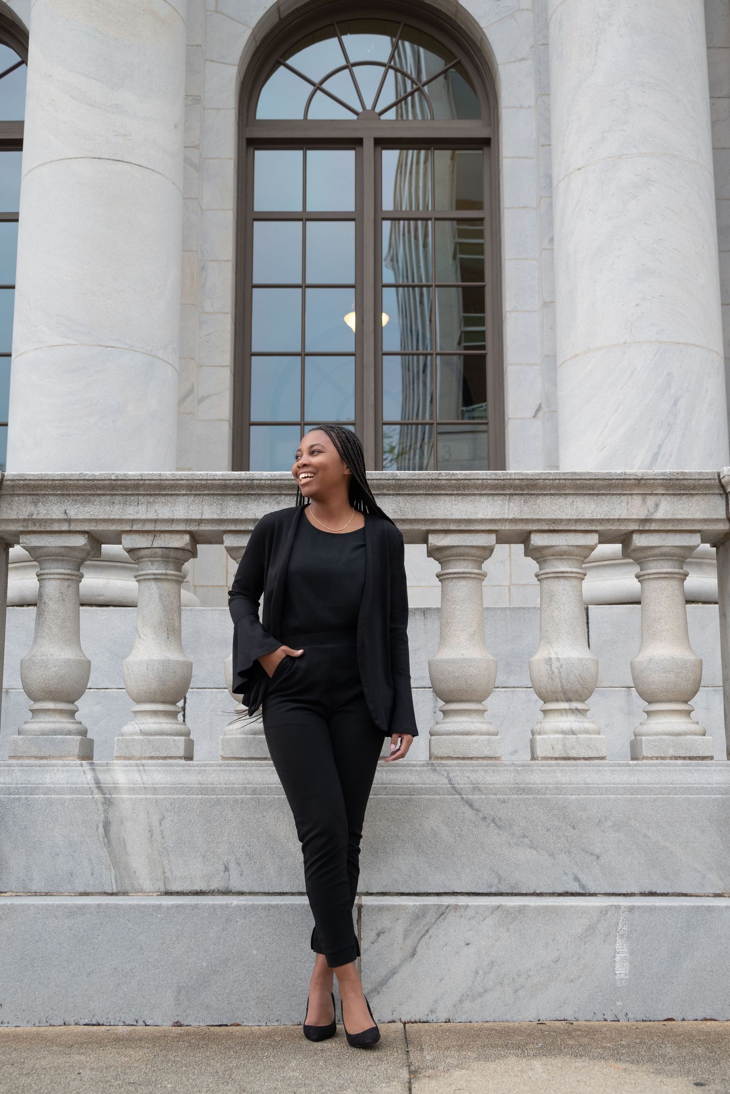 Stylish woman in all-black outfit standing near marble columns of a classic building.