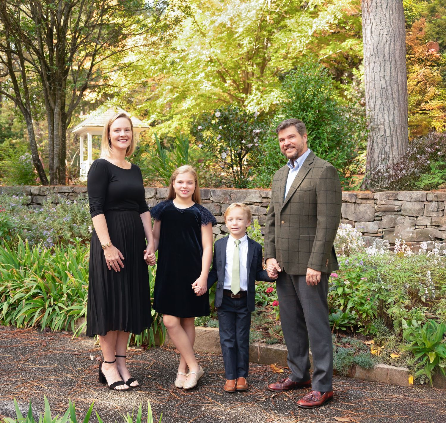 Family of four posing in a lush garden, dressed in formal attire, smiling for a portrait photo.