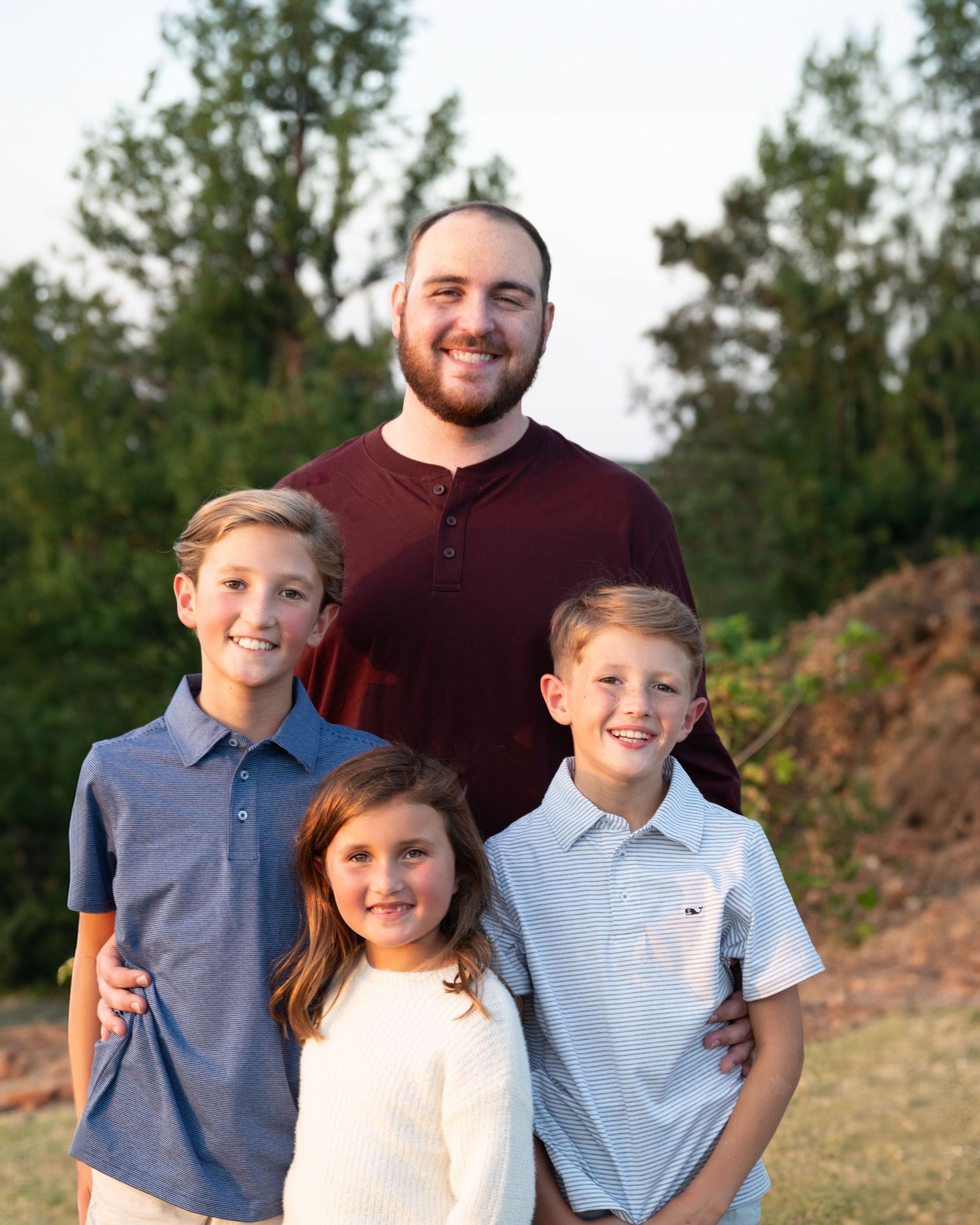 Young man with three younger siblings posing outdoors at golden hour in casual attire for a family portrait.