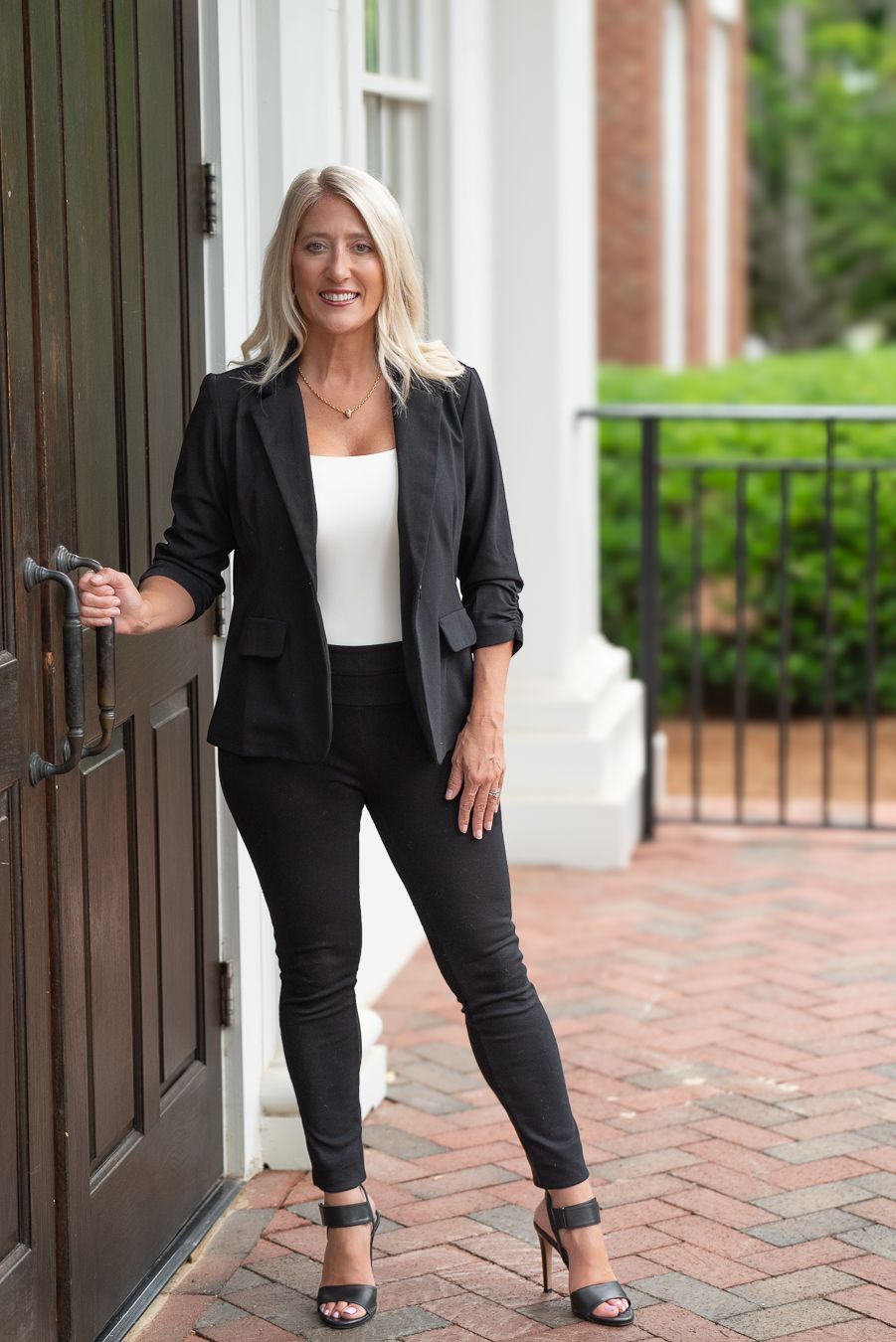 Professional woman in black blazer and pants posing at elegant building entrance.