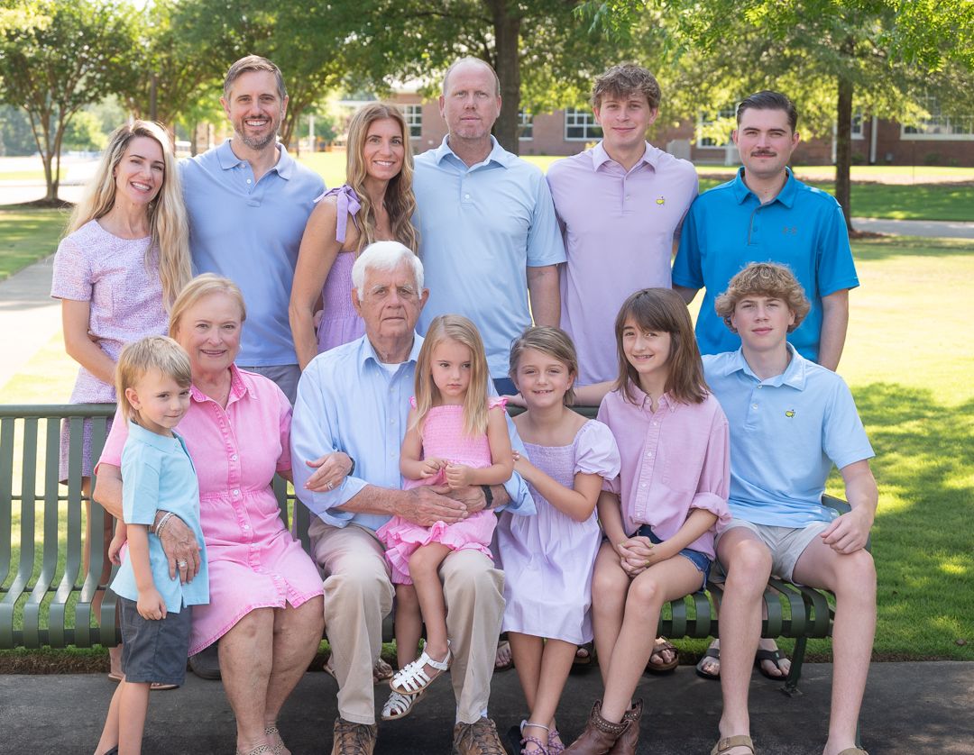 Large multigenerational family group portrait seated and standing together outdoors on sunny day.