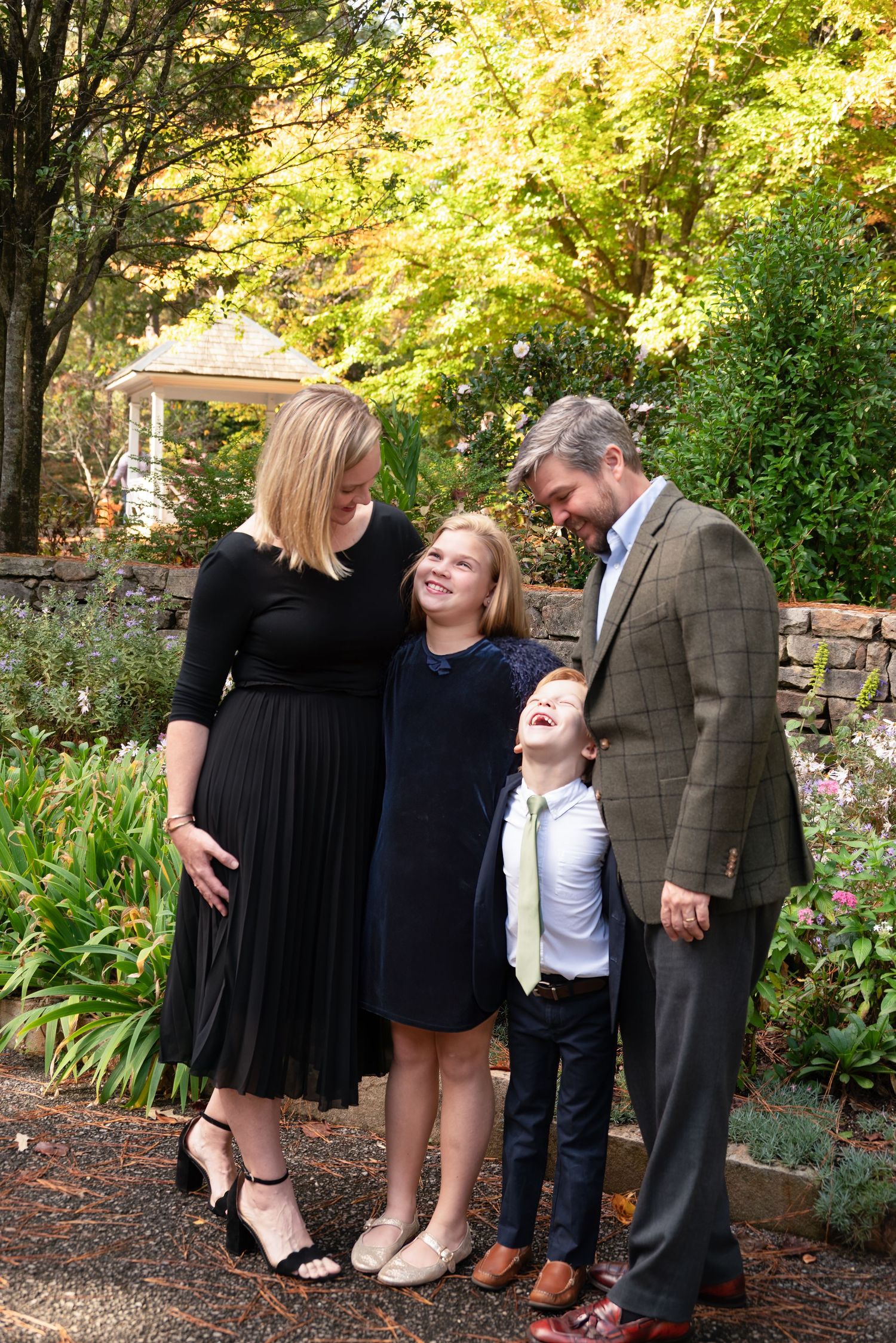 Family of four laughing together in a lush garden, parents and two children dressed in formal attire during autumn.