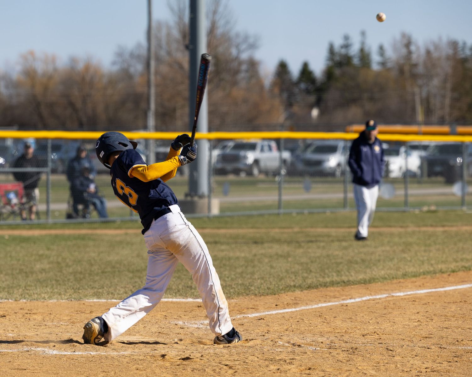 Young baseball batter swinging at a pitch during a sunny youth league game on a dirt infield baseball diamond.