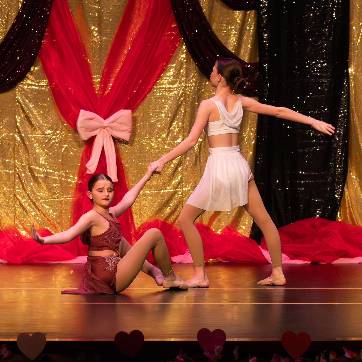 Two girls performing a contemporary dance duet on stage with gold sequin backdrop.