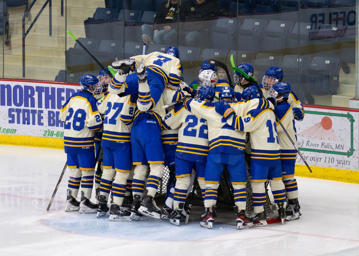Hockey team celebrates victory with a group huddle on the ice at Northern State Bank arena.