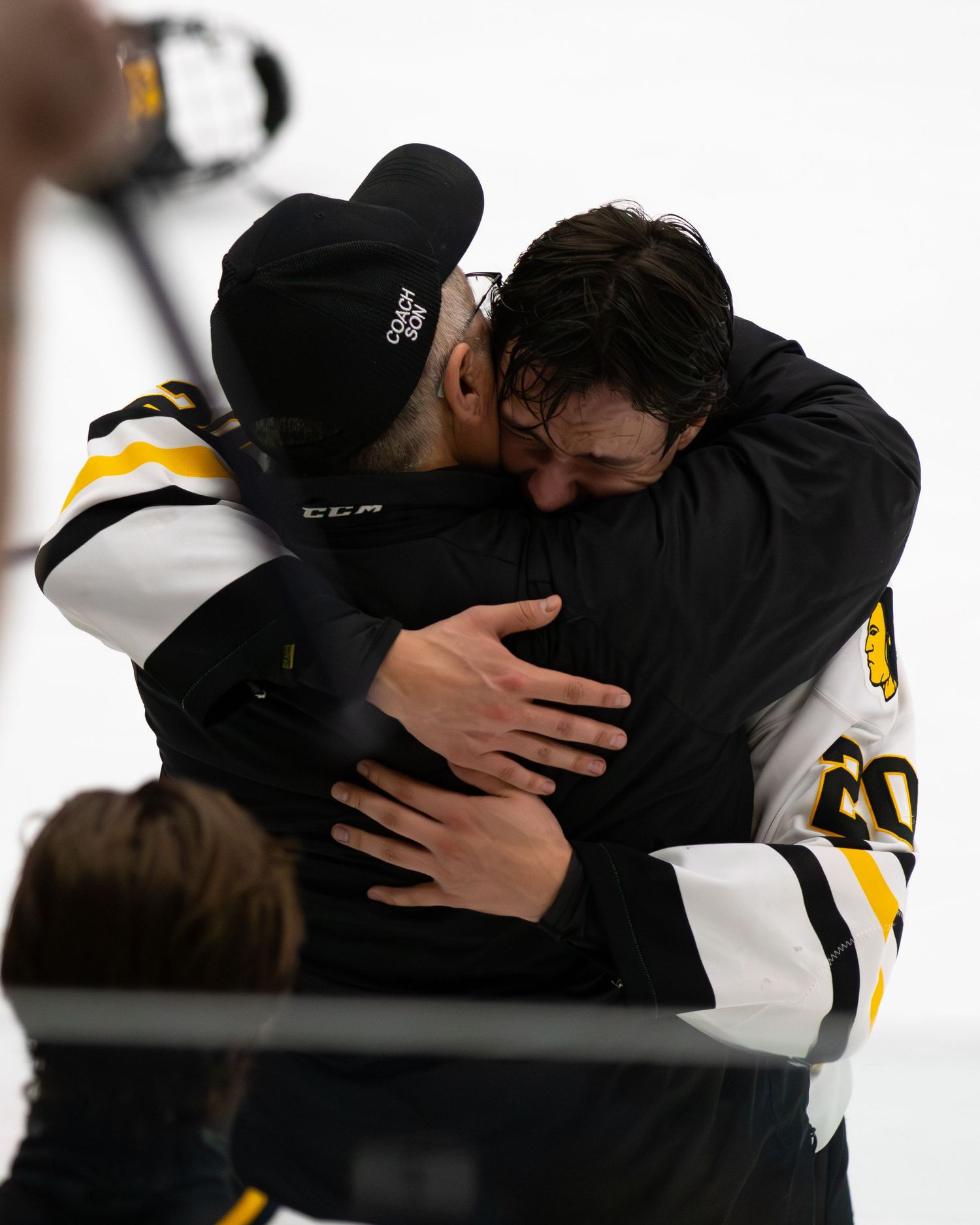 Two hockey players share emotional hug on ice rink after competitive hockey game ends.