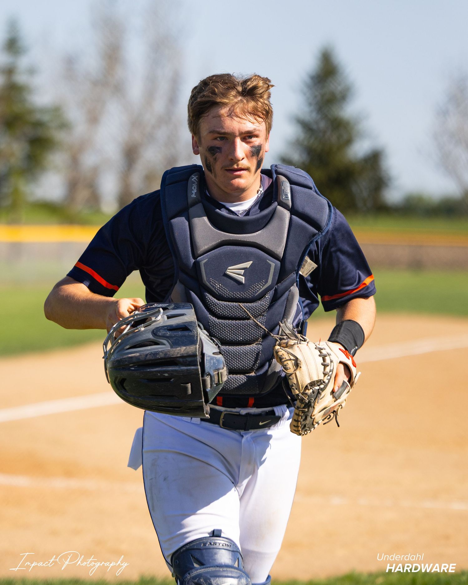 Baseball catcher in Easton chest protector and mitt runs on field during sunny game day.
