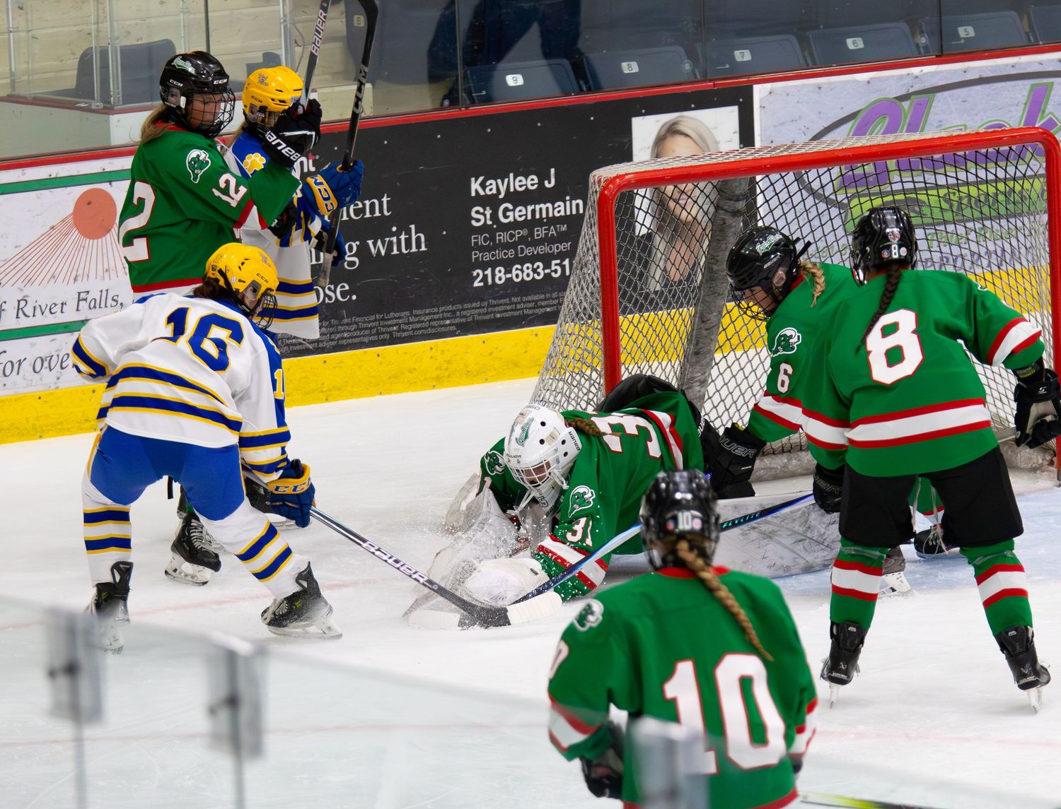 Girls hockey players battle for puck near Green team's goal on ice.