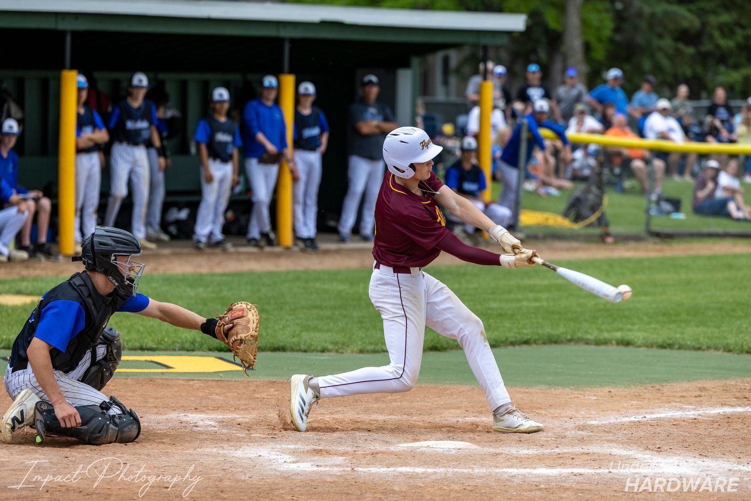 Youth baseball batter swings at pitch with catcher ready behind home plate during a sunny outdoor game.