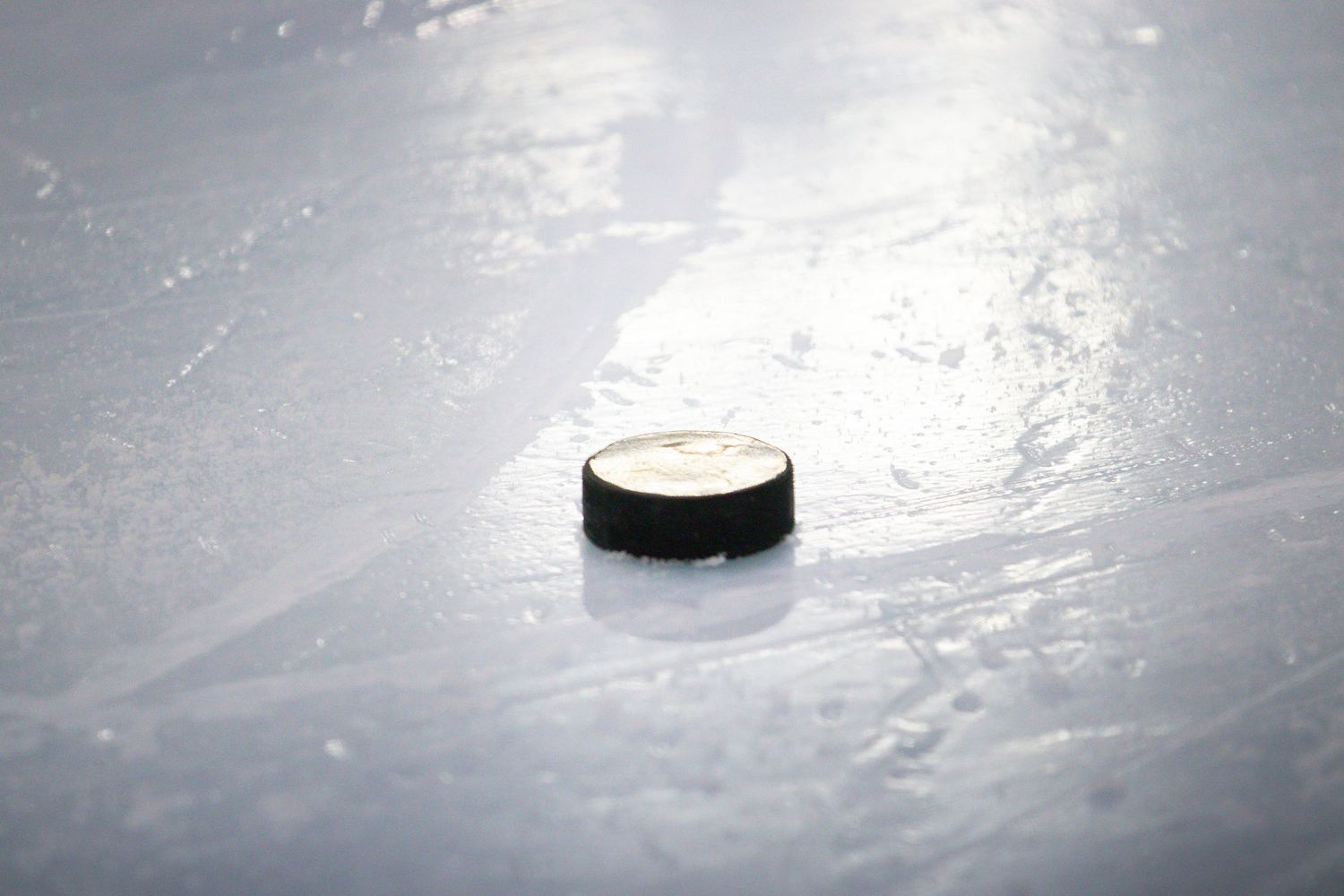 Close-up of a black hockey puck resting on white ice surface during a hockey game.