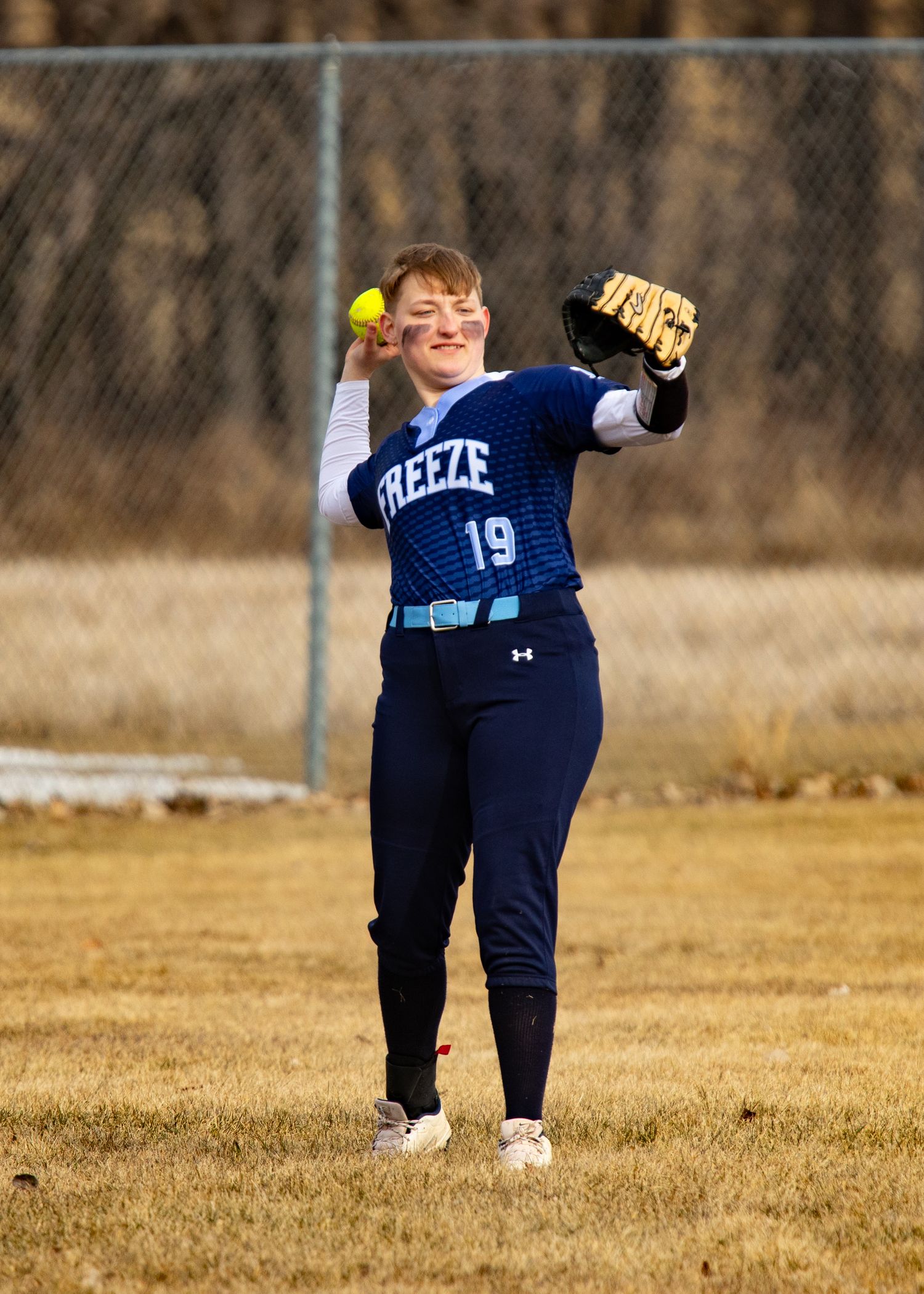 Softball player #19 in Freeze jersey throwing ball on field.