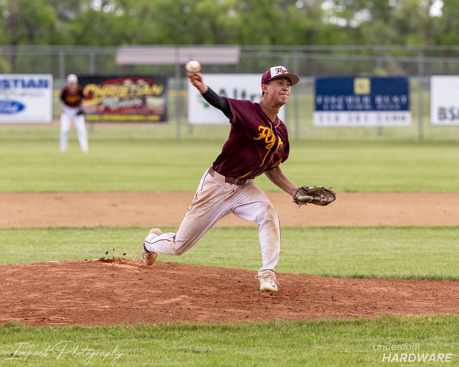A baseball pitcher in maroon and gold uniform delivers a pitch during an outdoor game on a green field.